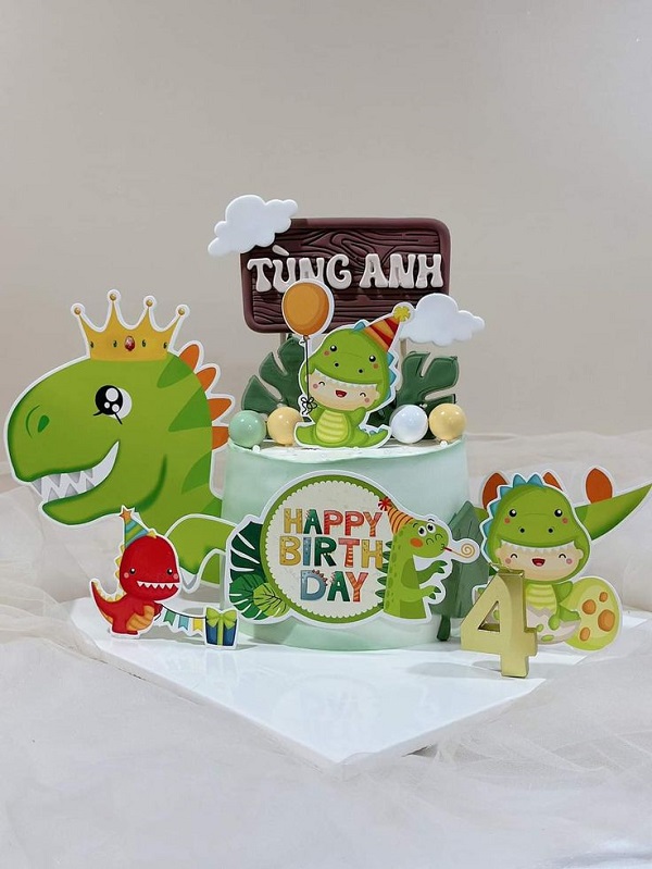Bánh kem hình khủng long ngộ nghĩnh với nền xanh và chữ Happy Birthday.