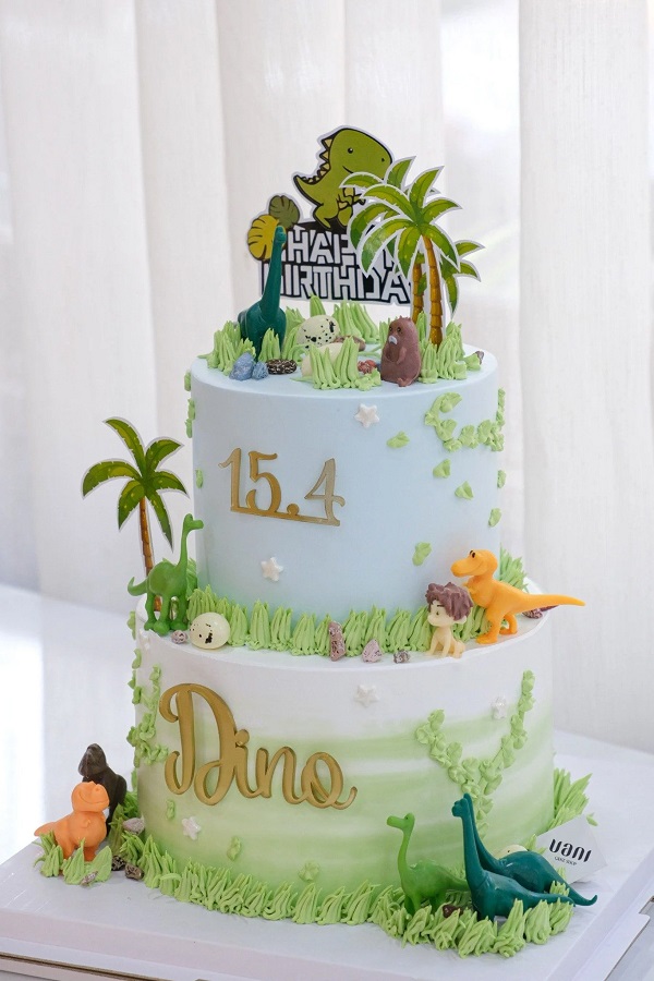 Bánh sinh nhật khủng long 2 tầng xanh lá với trang trí cây cối và trứng.